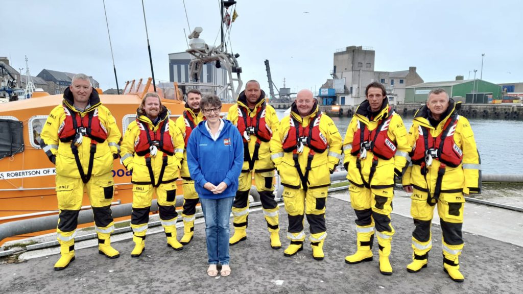 Christine stands proudly with 7 members of Peterhead RNLI in their yellow uniforms.