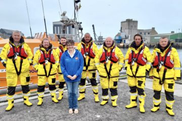 Christine stands proudly with 7 members of Peterhead RNLI in their yellow uniforms.