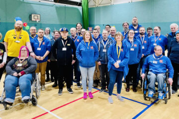 Group photo of all displayers and helpers inside sports hall, most wearing blue Tartan LUG hoodies.