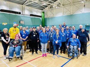 Group photo of all displayers and helpers inside sports hall, most wearing blue Tartan LUG hoodies.